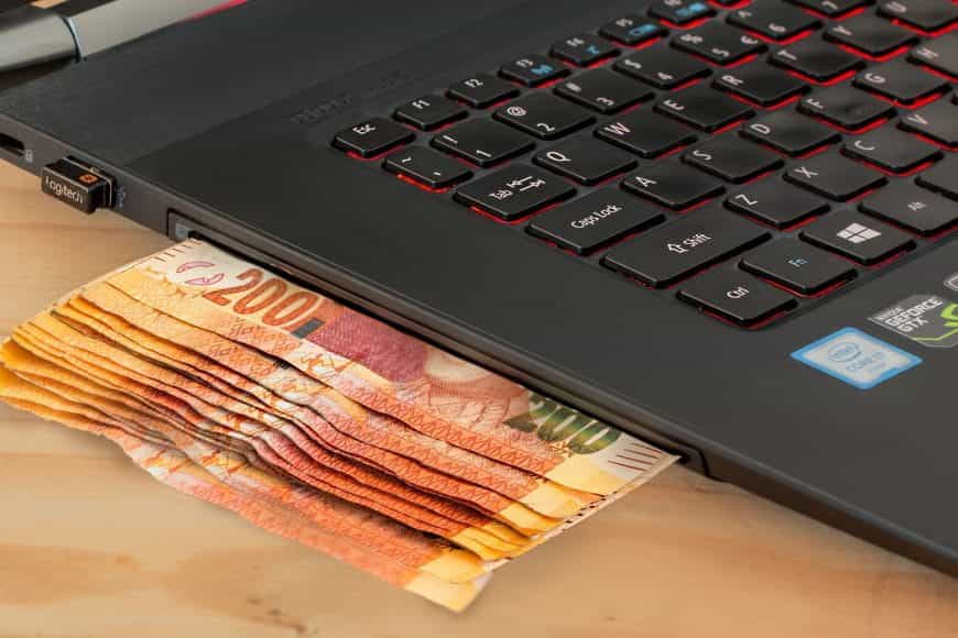 Mehrere Geldscheine stecken im Laufwerk eines Laptops.