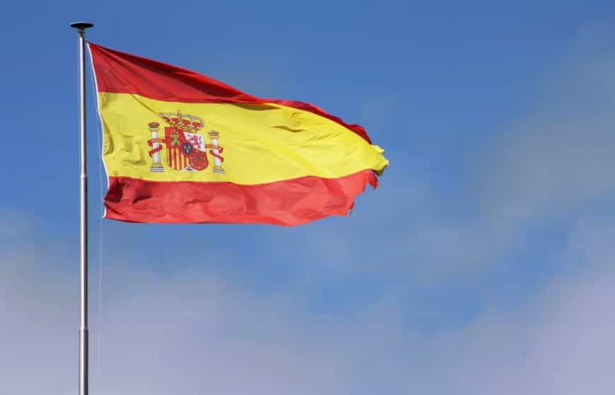 Spanische Flagge weht im Wind vor blauem Himmel.