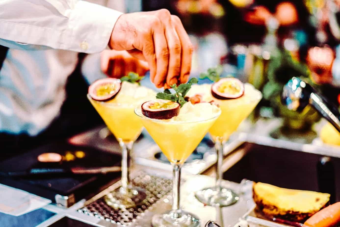 Hände verzieren 3 Cocktailgläser auf einer Bar-Anrichte.