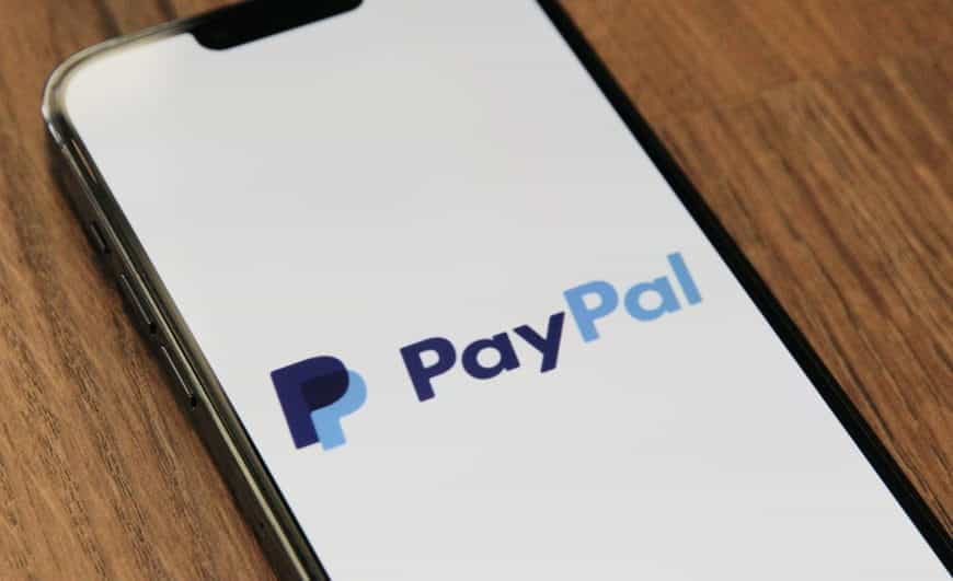 PayPal-Logo auf Smartphone-Display, das auf einem Holztisch liegt.
