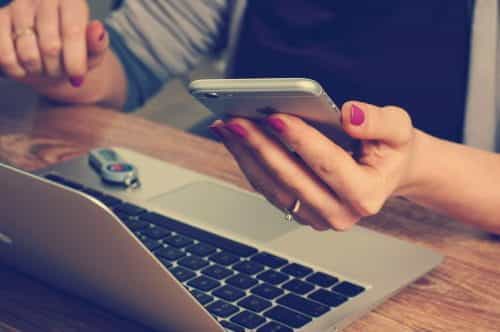 Frau zahlt mit iPhone und Apple Pay online am Notebook sitzend.