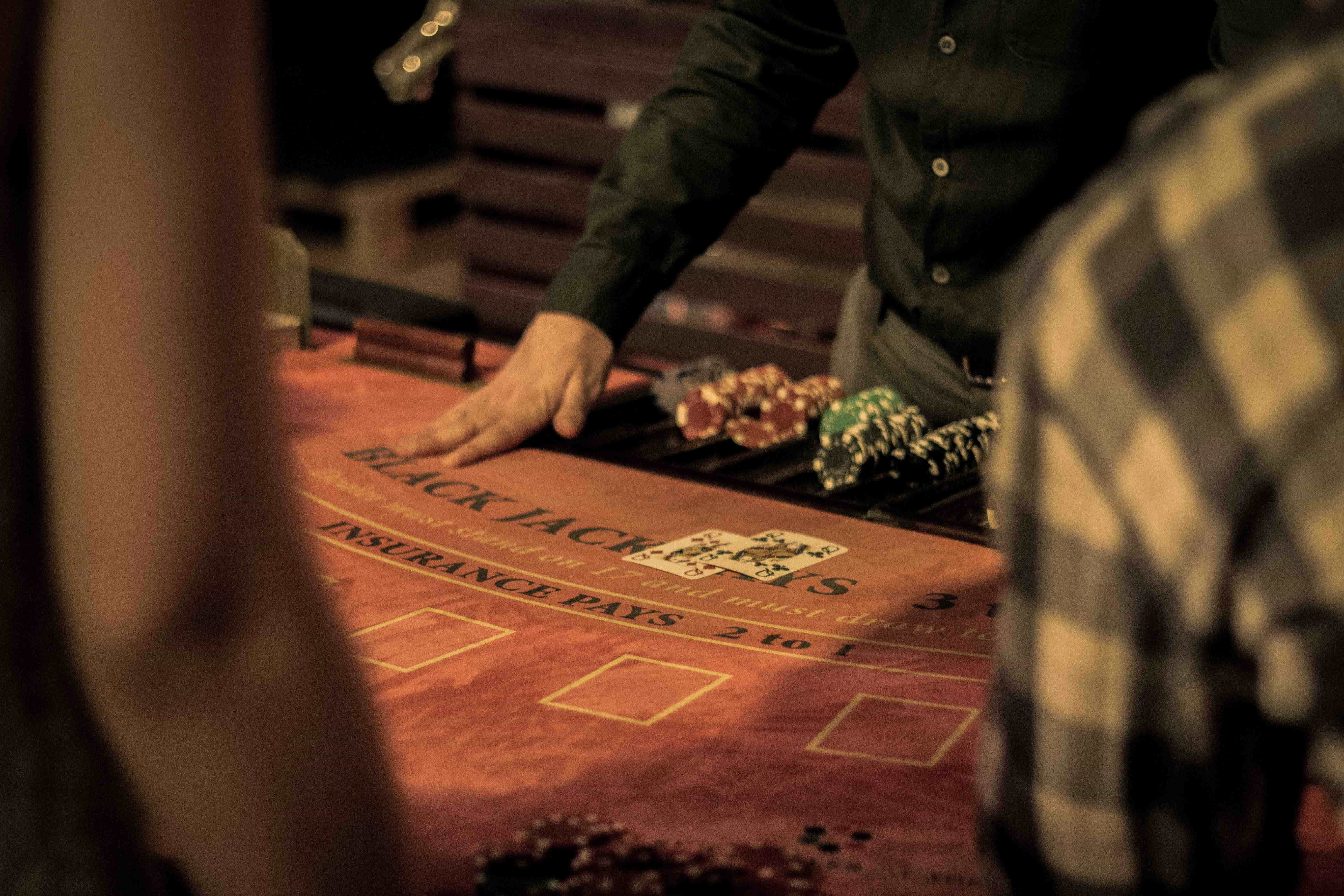 Ein Live-Dealer steht am Blackjack-Tisch im schwarzen Hemd vor einigen Jetons und ist dabei, Karten auszugeben.