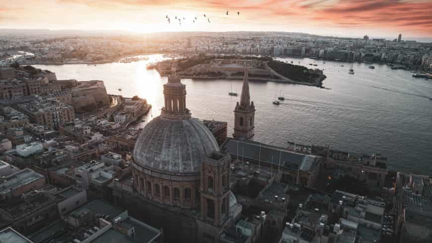 Panorama einer alten maltesischen Stadt bei Sonnenuntergang, in den Vögel hineinfliegen.