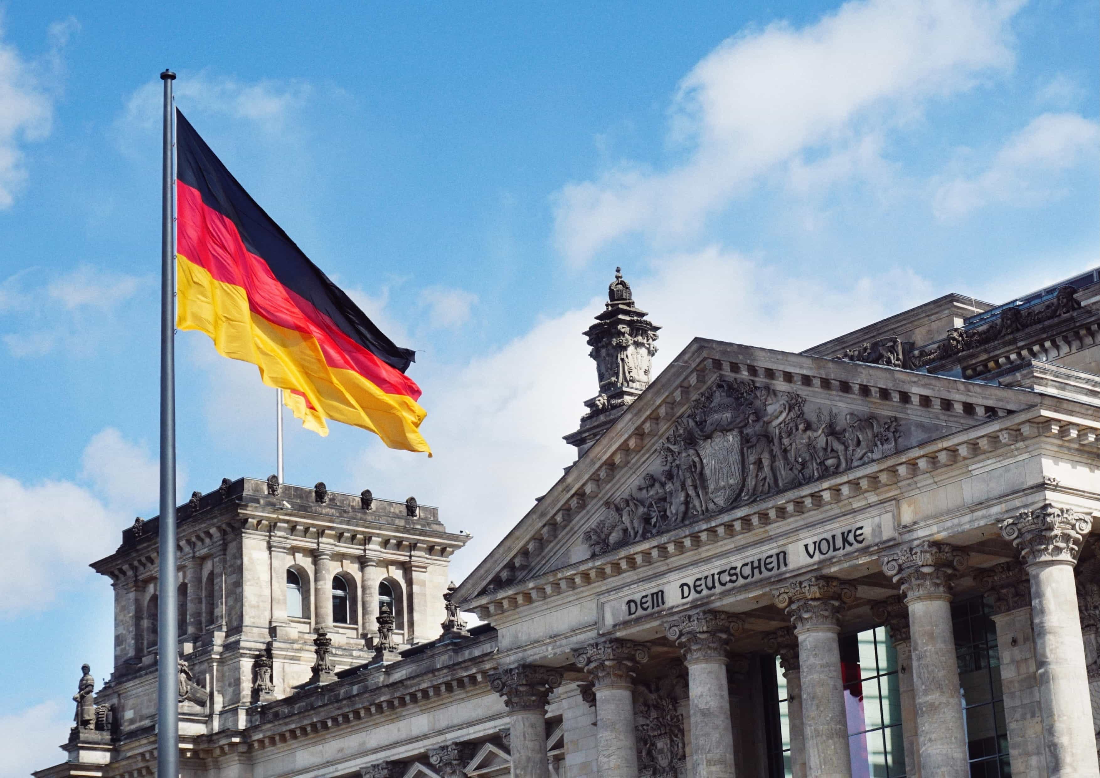 Bendera nasional Jerman berkibar di depan gedung Parlemen Jerman pada hari yang cerah dan biru cerah.