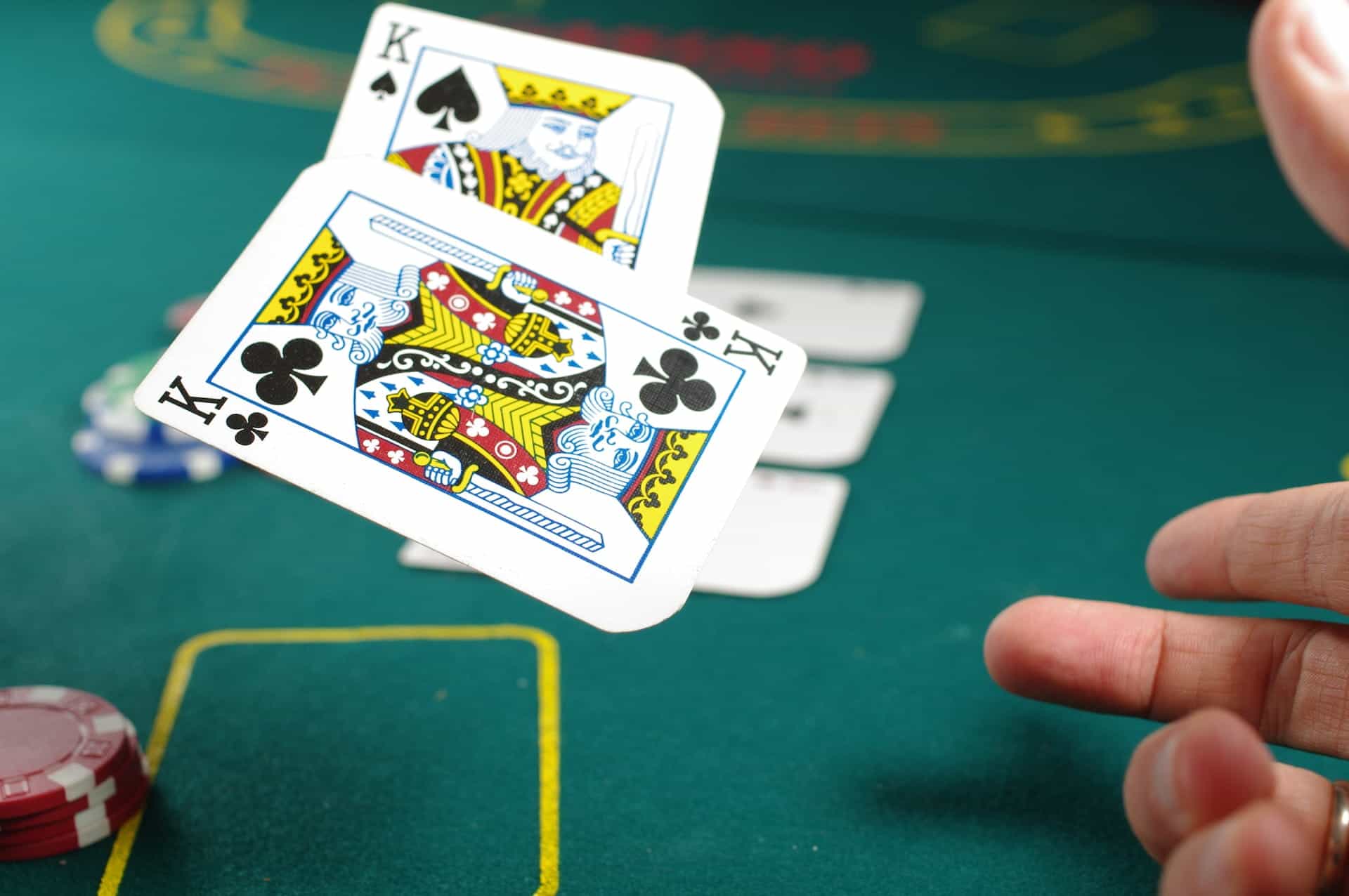 Ein Kreuz-König und ein Ass-König werden als Spielkarten von einer Hand auf einem Spieltisch im Casino in die Luft geworfen.