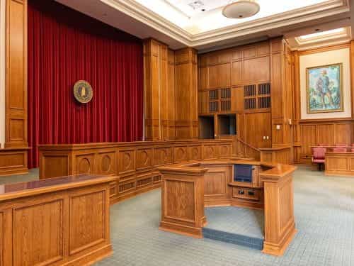 Leerer Gerichtssaal hell beleuchtet mit zahlreichen urigen Einrichtungsgegenständen aus Holz.