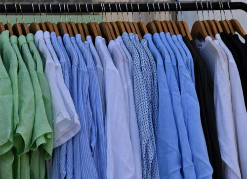 An einem Garderobenständer hängen mehrere Hemden und T-Shirts auf Kleiderbügeln.