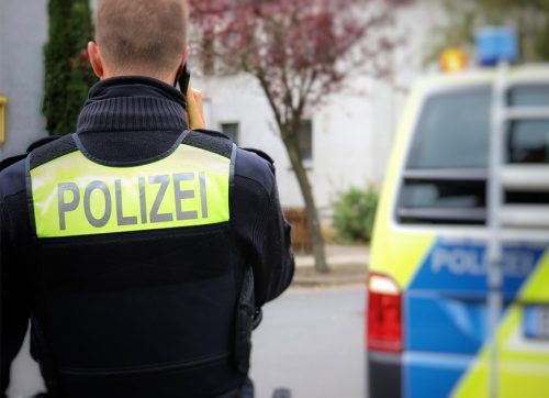 En Polizist telefoniert hinter einem geparkten Polizeifahrzeug.