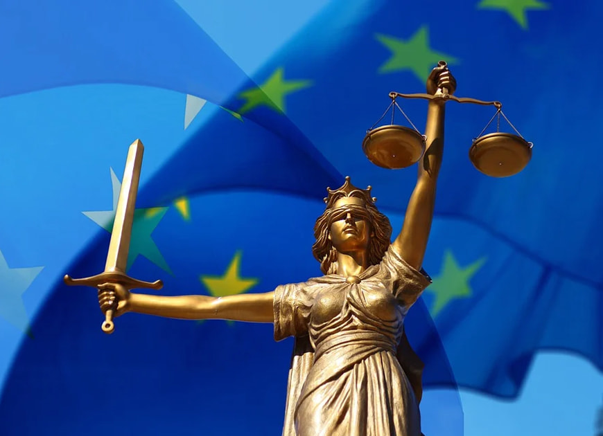 Eine goldene Justitia-Statue mit Schwert und Waage vor einer wehenden EU-Flagge.